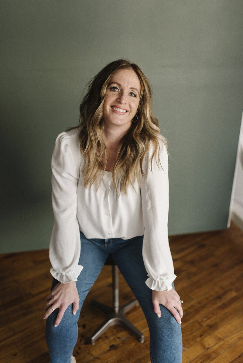 a woman dressed in a white top sitting on a stool