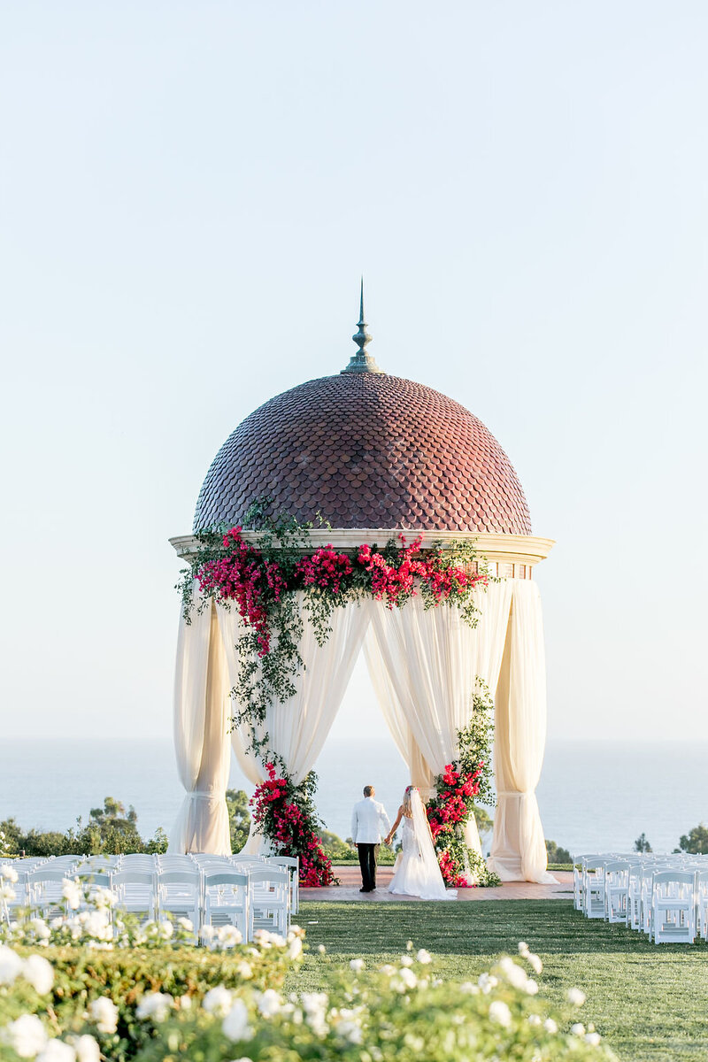 Bride & Groom walking under Ceremony Rotunda with pink bougainvillea floral installation at Pelican hill Resort