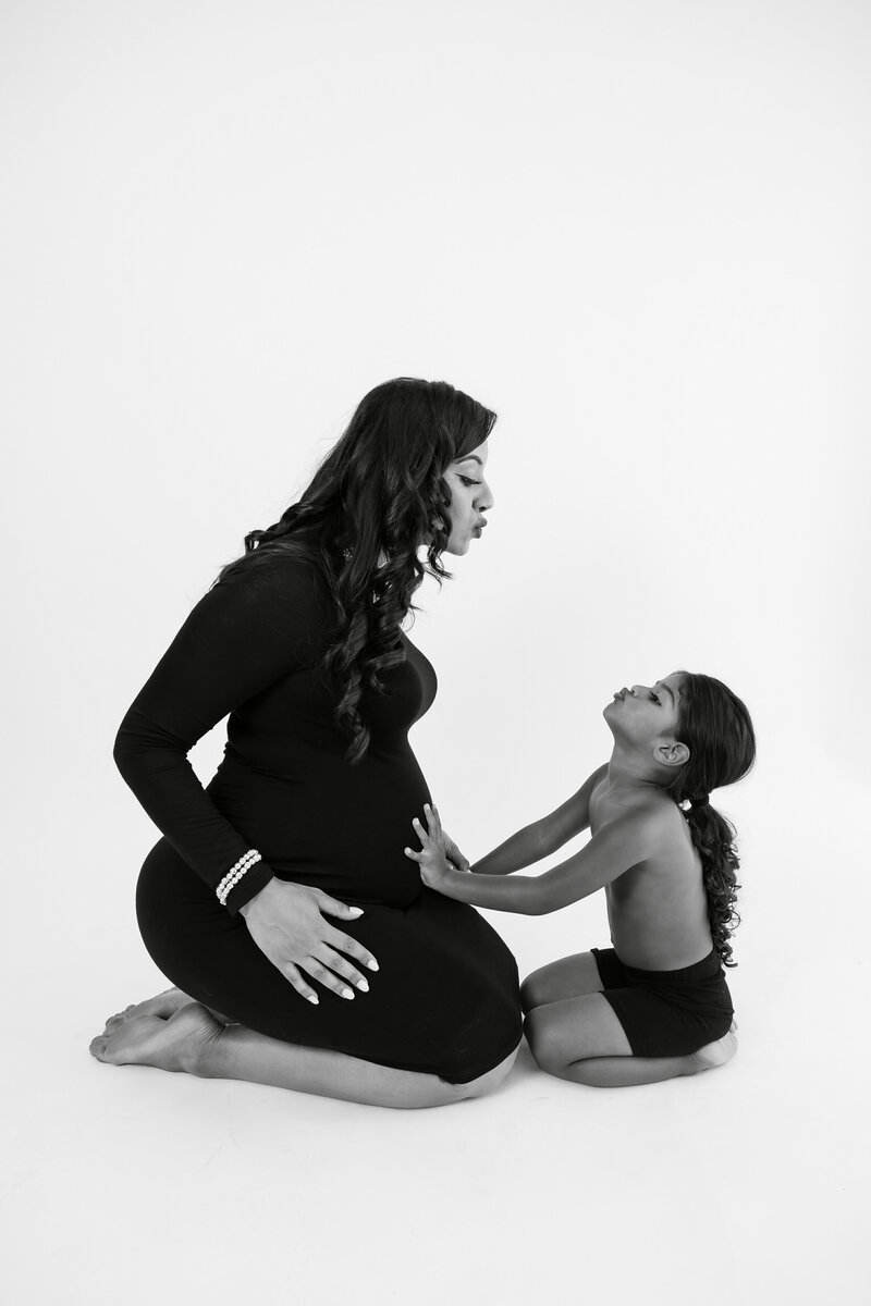Black and white portrait of pregnant mother and child making kiss faces at each other while toddler has hands on her belly