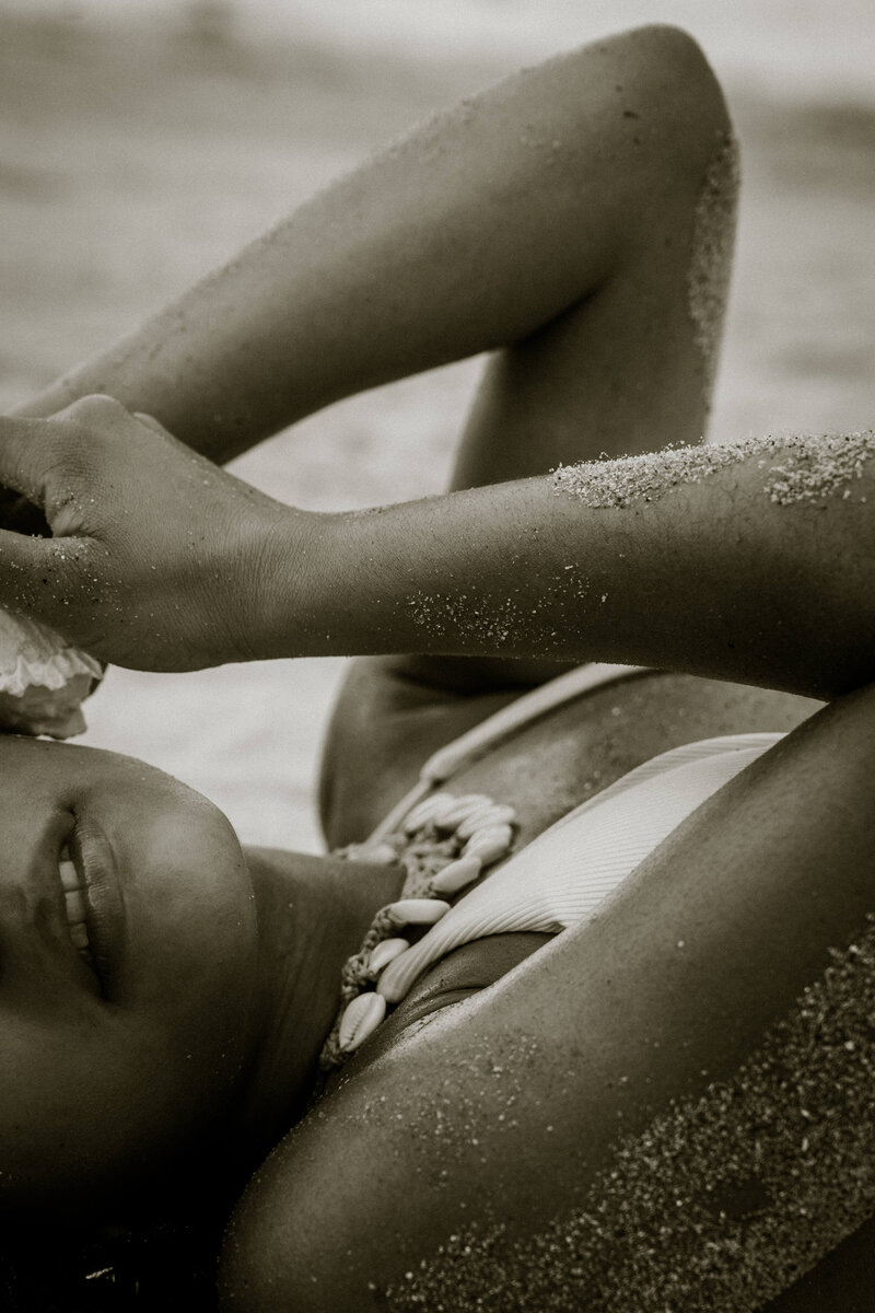 Model laying on beach with shell