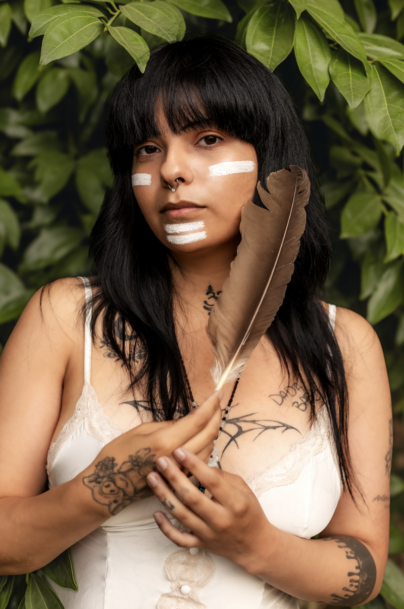 a queer indigenous person poses with a feather during a self love portrait session
