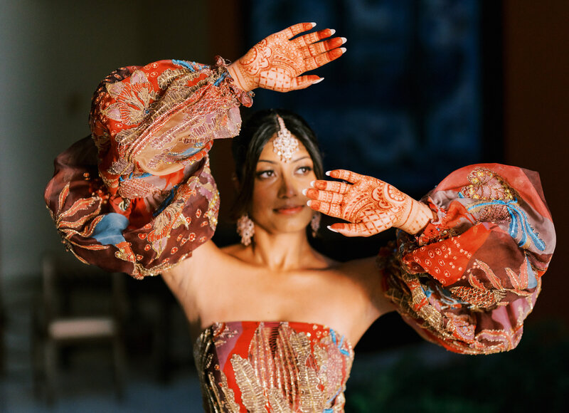 A woman dressed in traditional South Asian attire with intricate henna tattoos displayed on her hands, wearing ornate jewelry and a vibrant outfit. This image reflects the cultural beauty often incorporated in destination weddings.