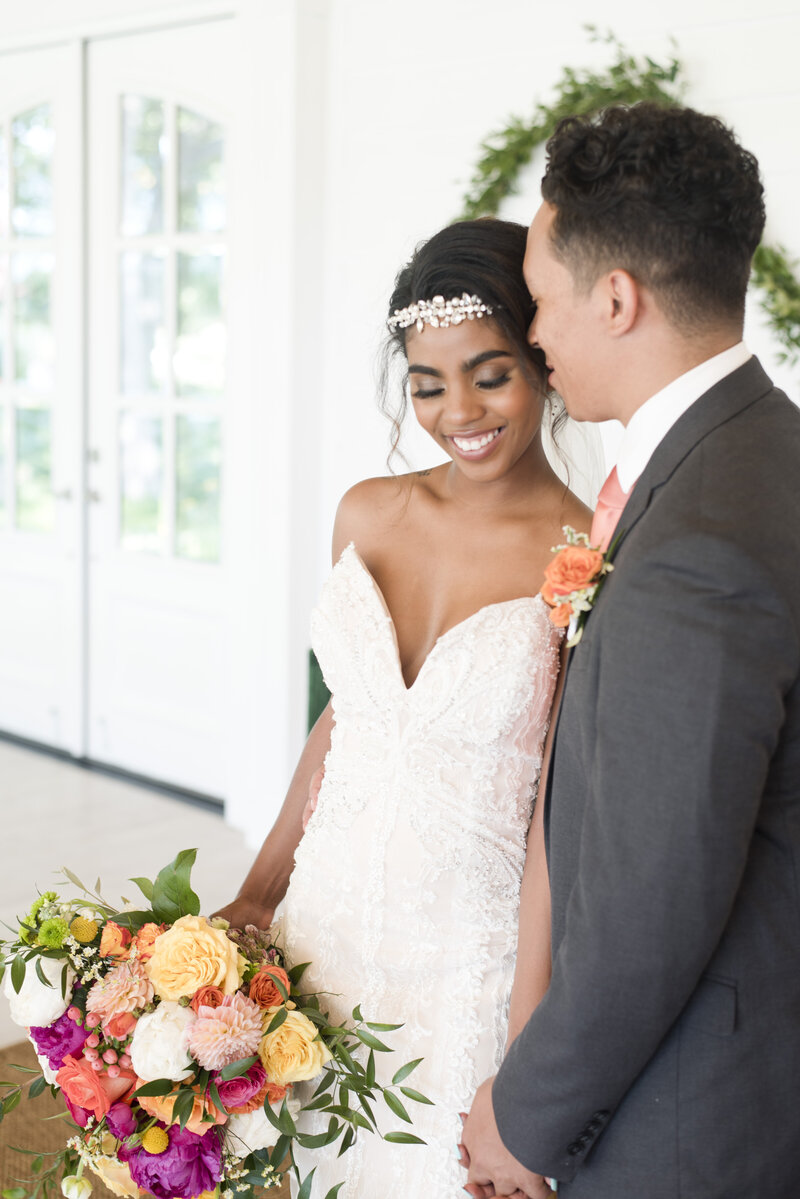 Groom kissing brides head as she holds colorful bouquet in Fort Worth Texas