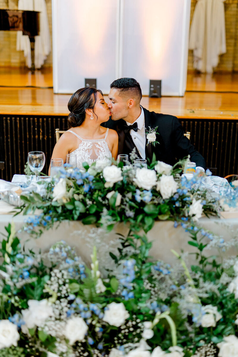 Bride and groom kissing at sweetheart table with floral décor