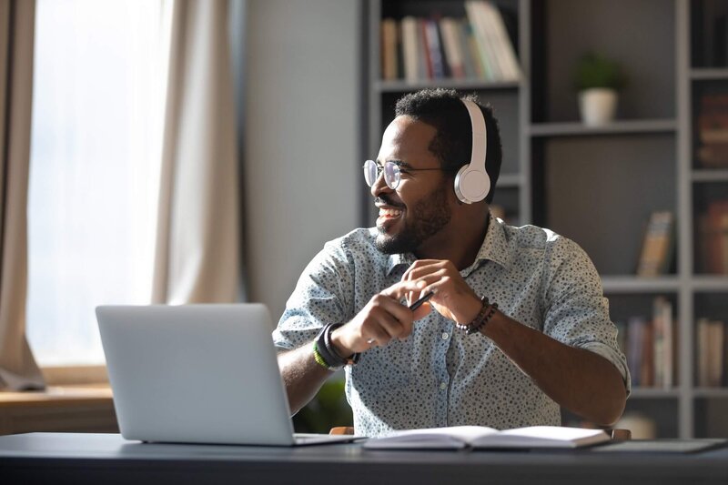 Man with headphones looking out the window at a desk smiling