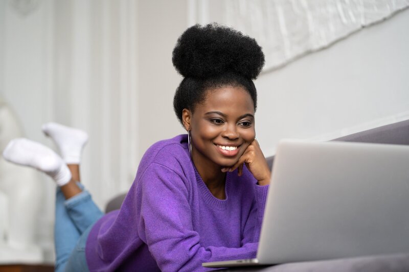 smiling-african-american-millennial-woman-with-afro-hairstyle-wear-purple-sweater-lying-on-sofa_t20_gL460G