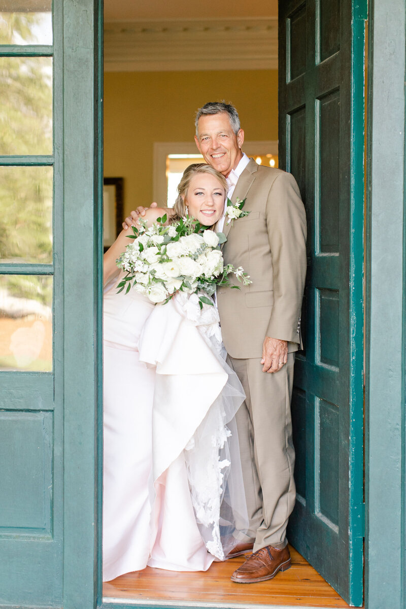 bride and father of the bride standing next to green door smiling and h