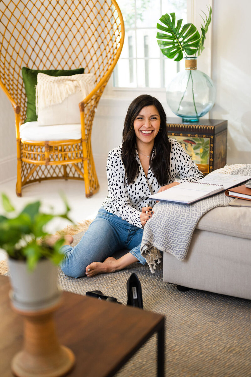 Karen, a real estate agent, sitting on the floor as her notebook rests on the couch  with a rattan peacock chair in the background