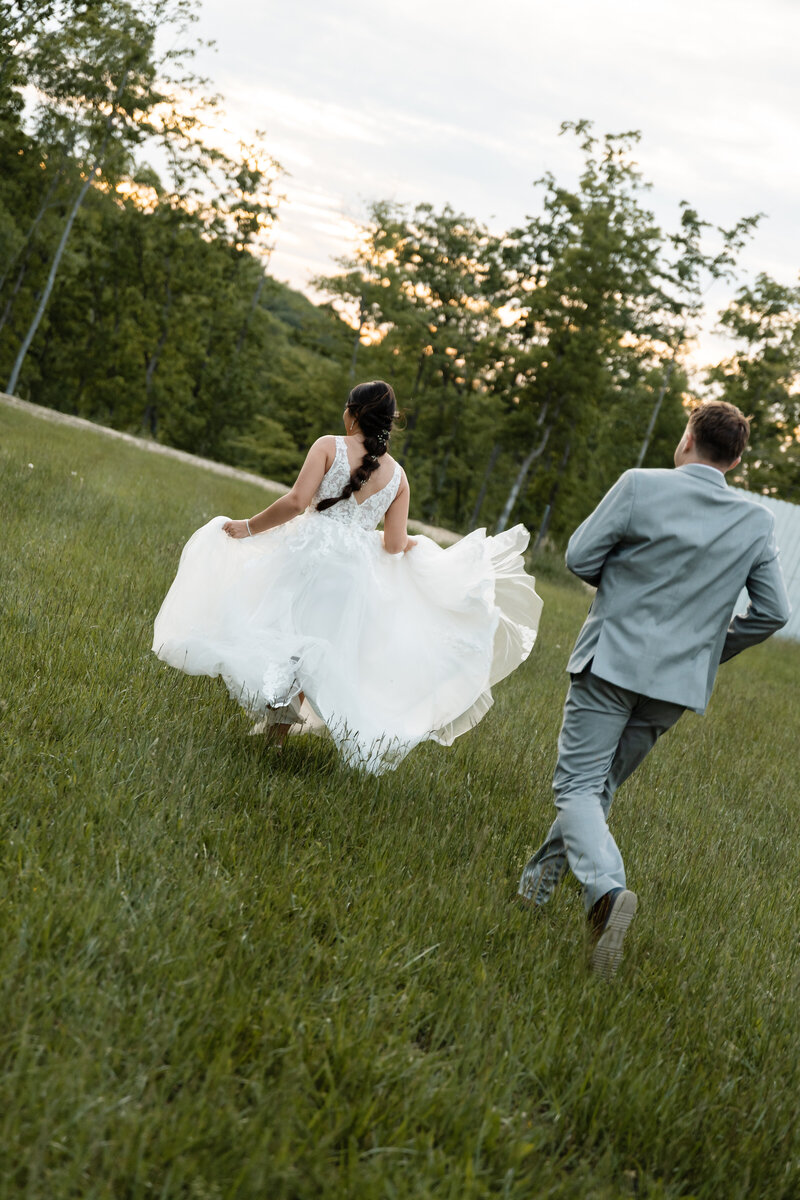 Wedding couple running hand in hand through an open field, captured in a carefree and joyful moment filled with laughter and love.