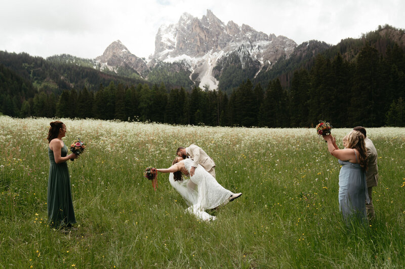 Dolomites Elopement Ceremony, groom dips bride for her first kiss with a mountain background while guests cheer