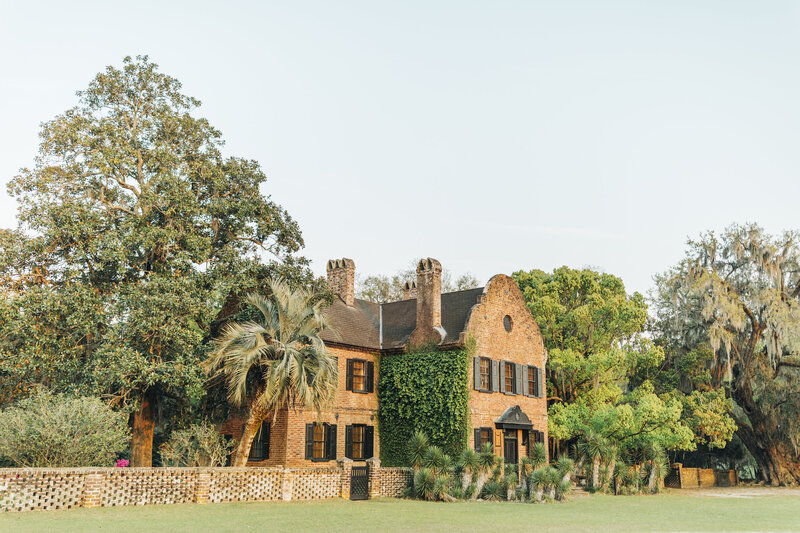A historic brick house at Middleton Place in Charleston, draped in ivy and surrounded by lush greenery and towering oak trees, capturing the essence of timeless Southern charm
