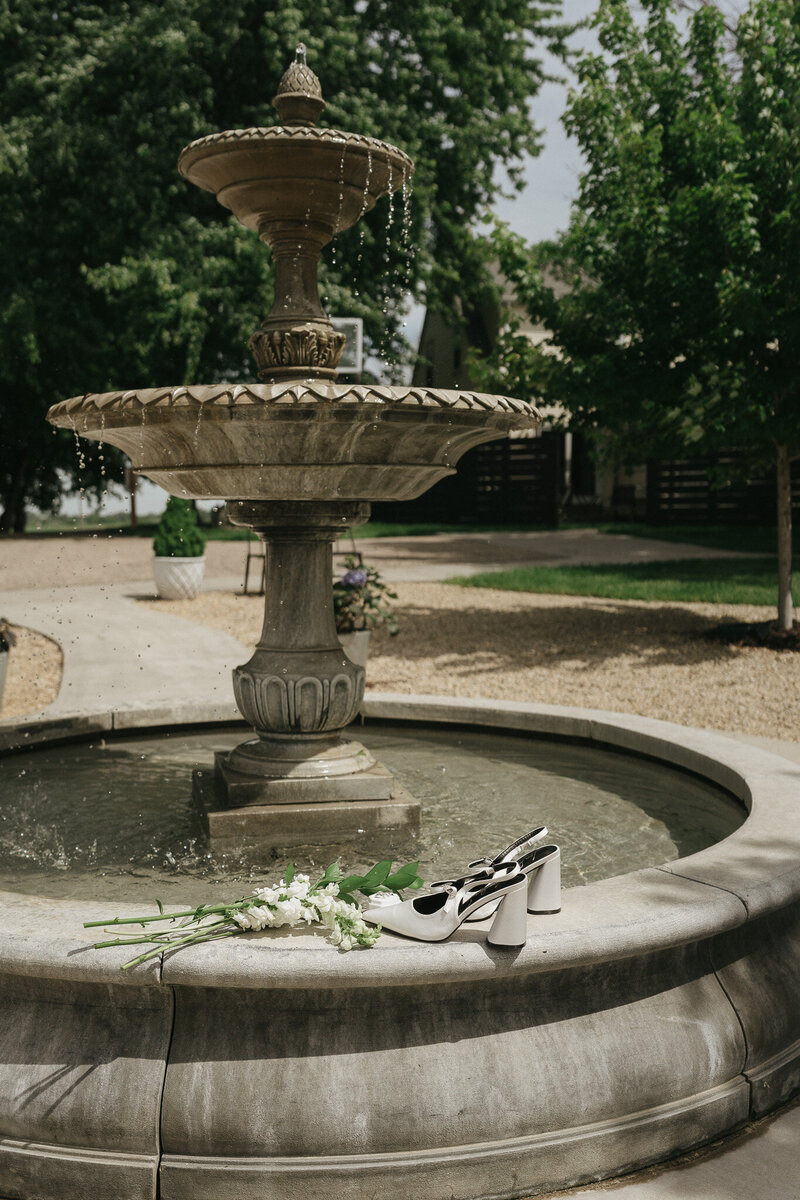 A pair of heels and flower bouquet sit on the edge of a fountain.