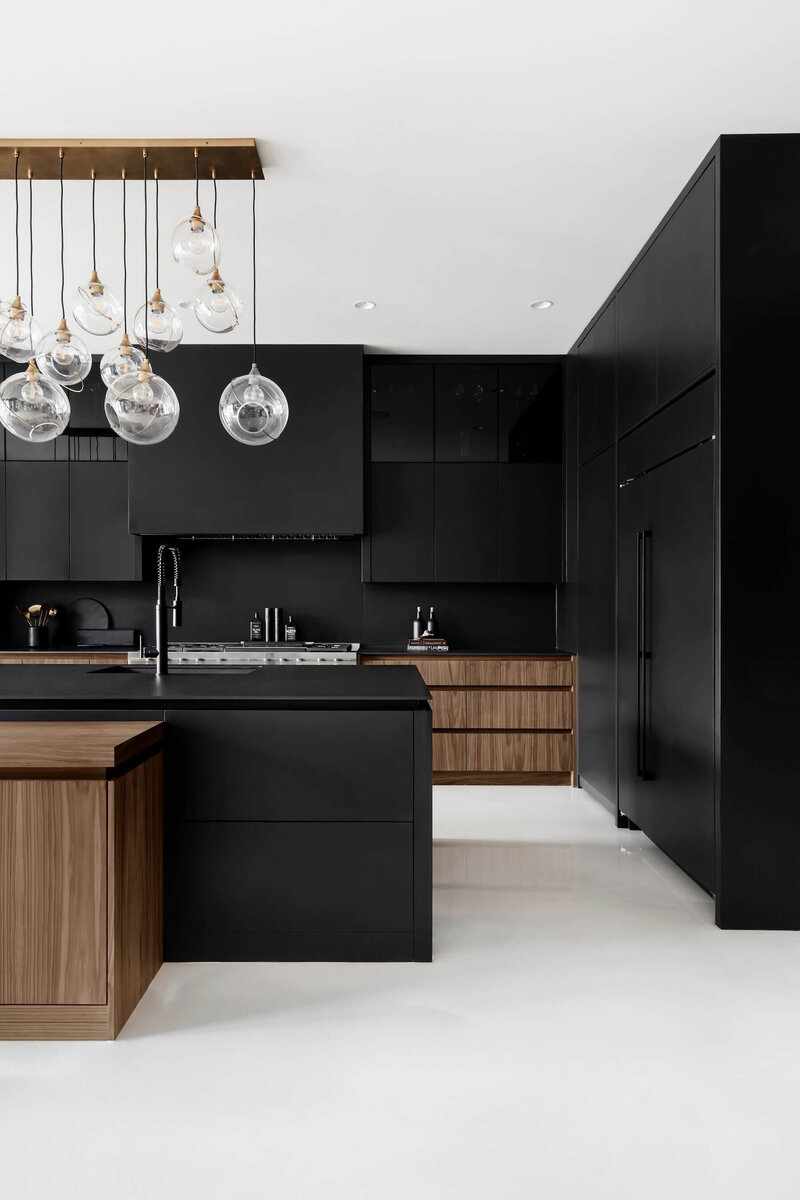 A black and walnut kitchen paired with epoxy floors and oversized glass pendants. 