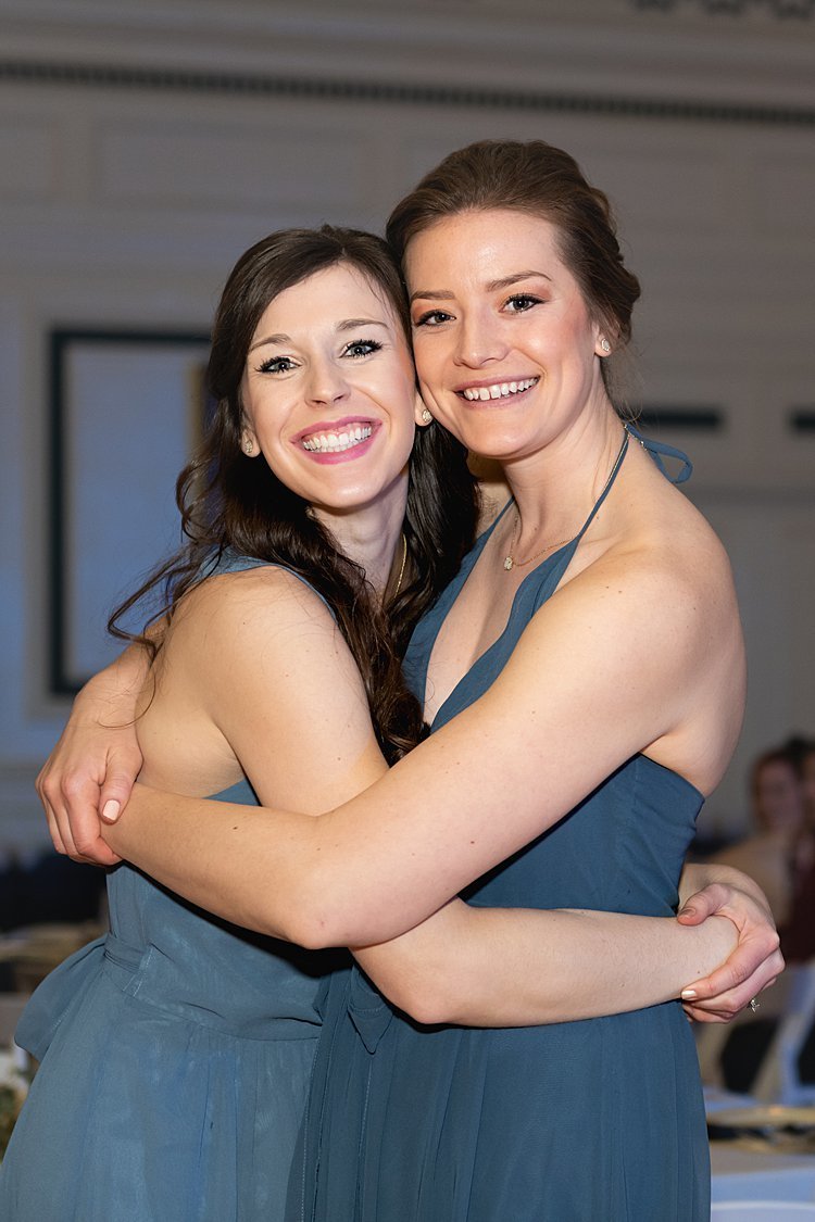 Two bridesmaids wearing cornflower blue dresses hugging at Soldier and Sailors Memorial Hall in Pittsburgh, PA