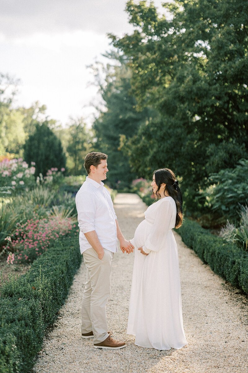 a husband and wife hold hands and stare lovingly at each other while expecting their first child and celebrating at Nemours Mansion and Gardens during their photo session with philadelphia maternity photographer