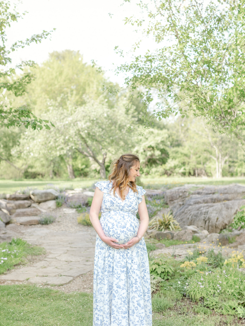 pregnant woman wearing blue floral dress cradles baby bump and smiles while looking over her shoulder