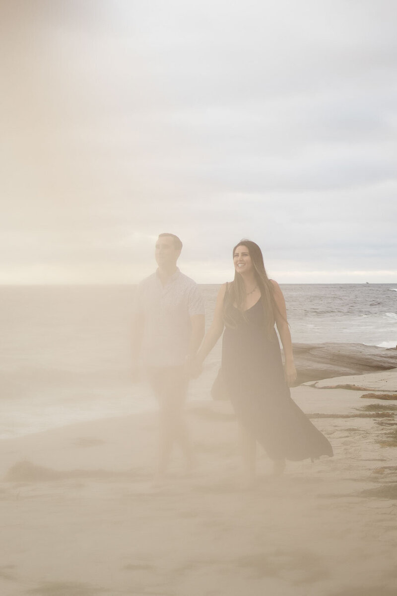 Couple walking hand-in-hand on the beach, surrounded by a soft mist