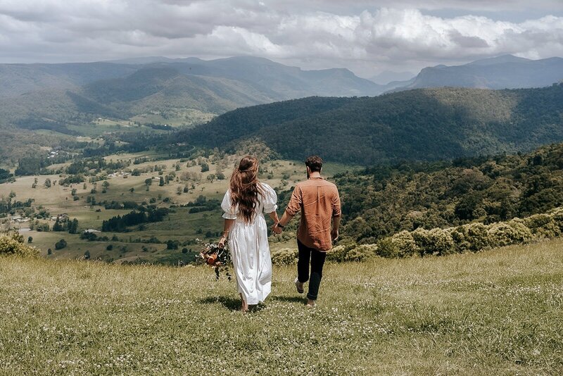 A bride and groom holding hands on a mountain top overlooking the hinterlands