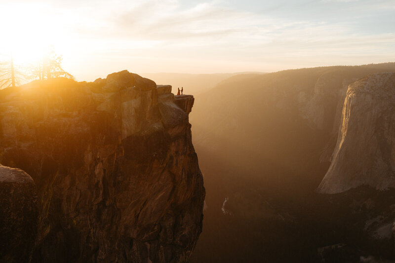 Yosemite elopement at Taft Point the couple is standing on the edge of a cliff with the sunset behind them