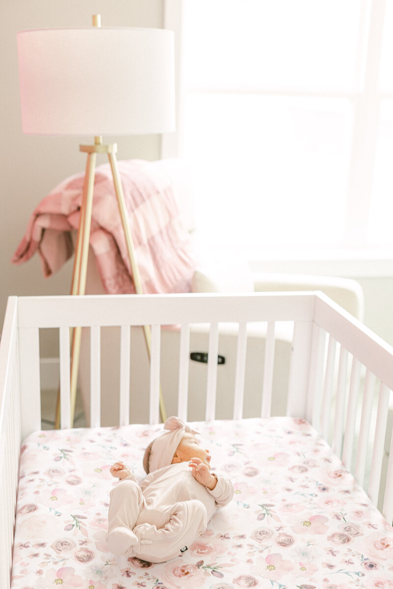 A newborn baby lying in a white crib in a sun-filled nursery decorated in pink
