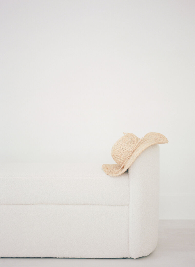 A straw hat sitting on a white fur bench in all white studio by NJ photographer