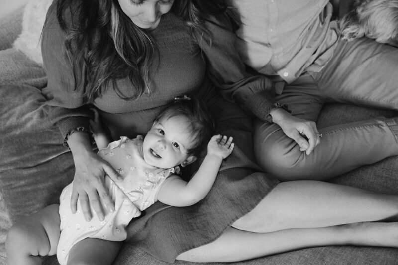 toddler lays on mom's lap during family session while hanging on their couch