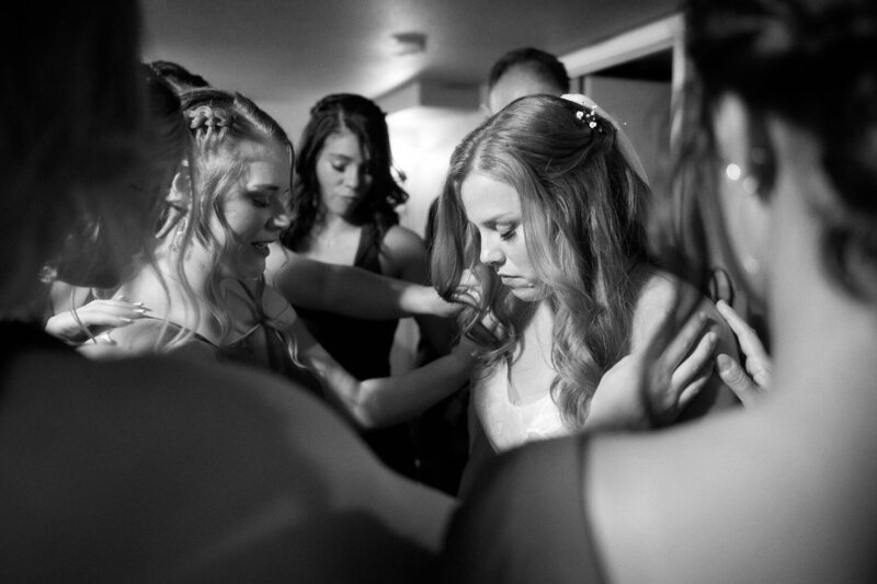 Bridesmaids all place their hands on the bride for a pre-ceremony private prayer