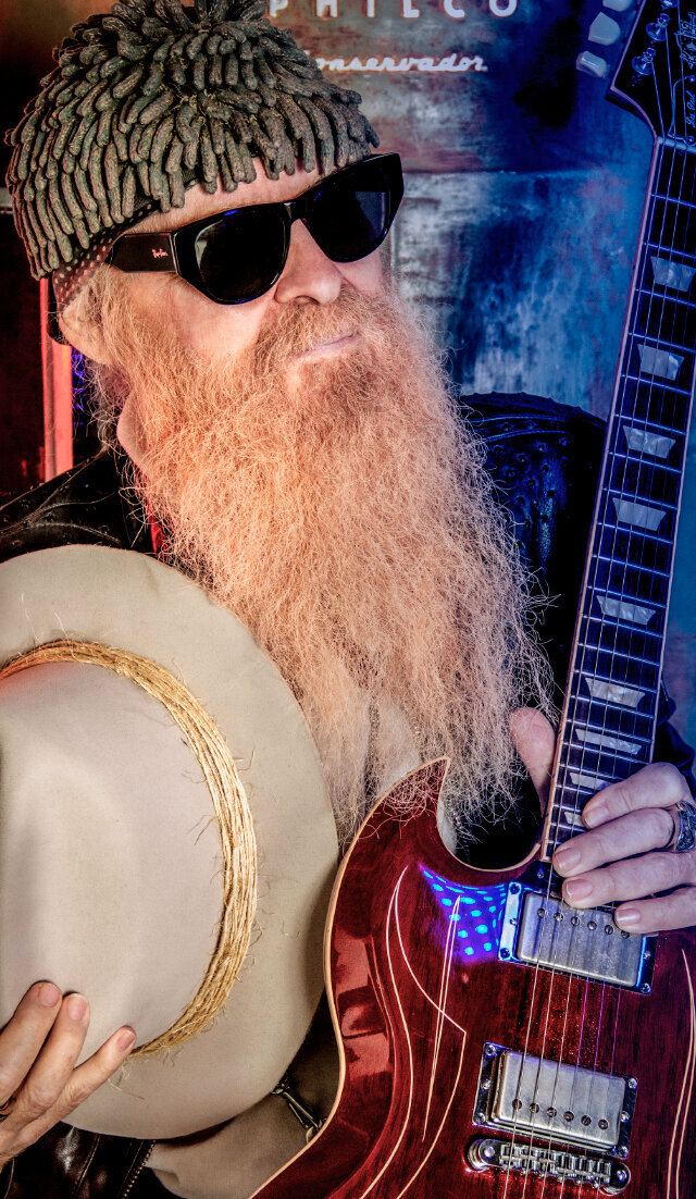 Music portrait Billy Gibbons holding red guitar and white cowboy hat wearing sunglasses
