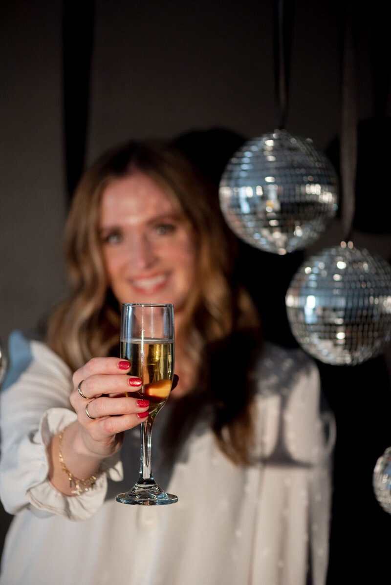 Woman holding champagne glass in front of disco balls