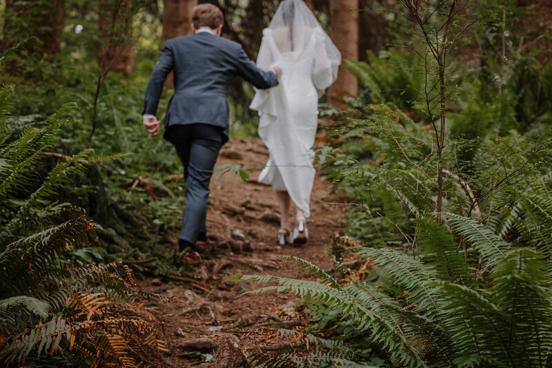 Bride and groom hiking up a trail through ferns