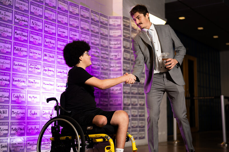 a hockey athlete shaking hands with a teenage pediatric cancer warrior