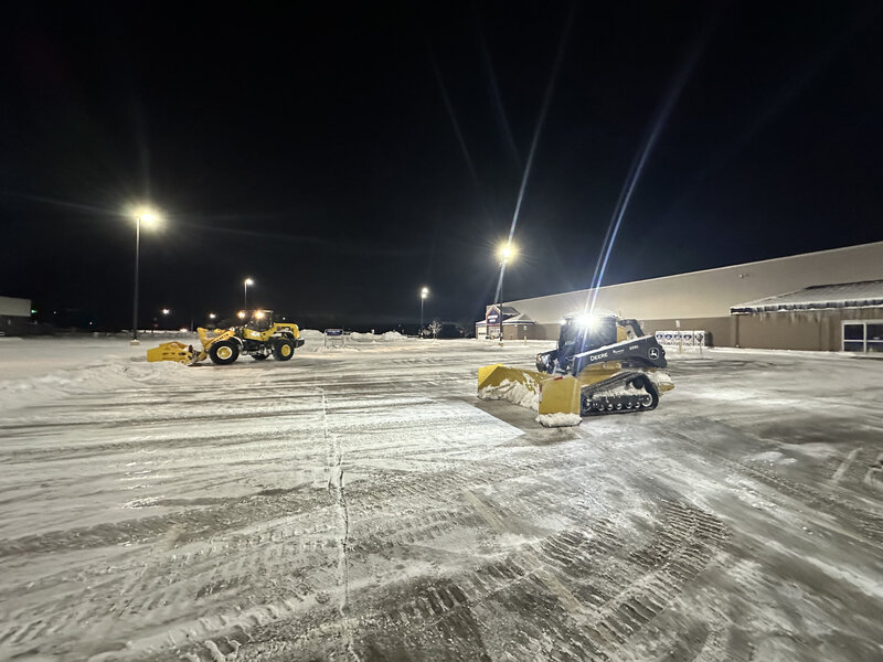 Commercial snow plowing services at night with multiple yellow snowplows in a cleared parking lot