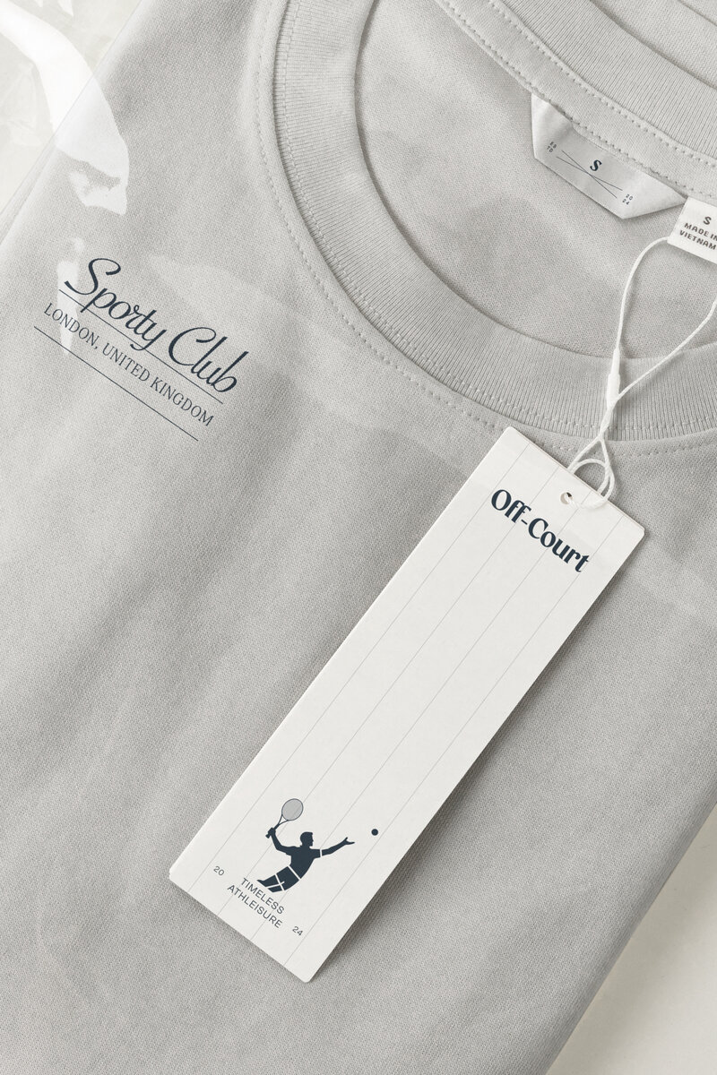 Off-Court brand identity on light gray t-shirt with sporty club typography and branded tag featuring tennis illustration.