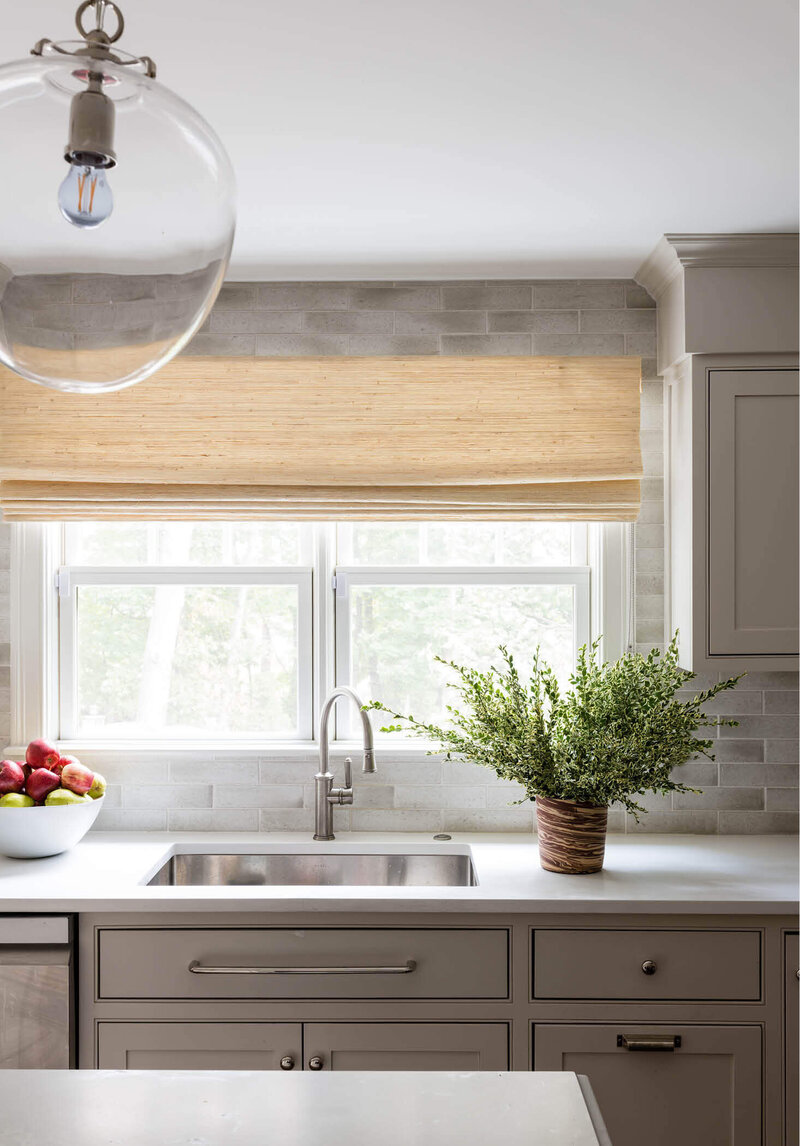 Milton kitchen designer creates a simple white kitchen with an artisan tile backsplash, Caesarstone counters, glass pendants from Visual Comfort, and woven wood shades.