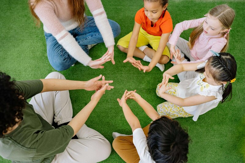 teacher and children in a circle holding out their hands