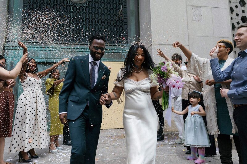 nyc city hall elopement couple with purple spring bouquet and reformation dress throwing confetti