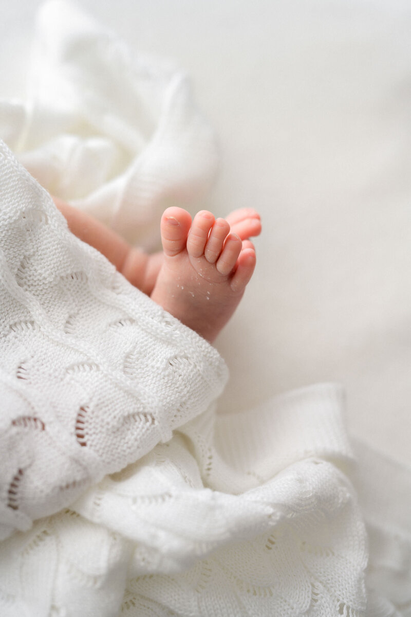 Close up of baby toes peeking out of delicate white baby blanket