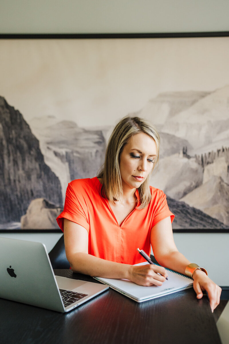 woman in orange blouse writes on paper during boston brand photoshoot
