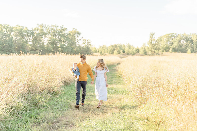parents walking with baby in the middle of a field during fall mini session in Leesburg, VA
