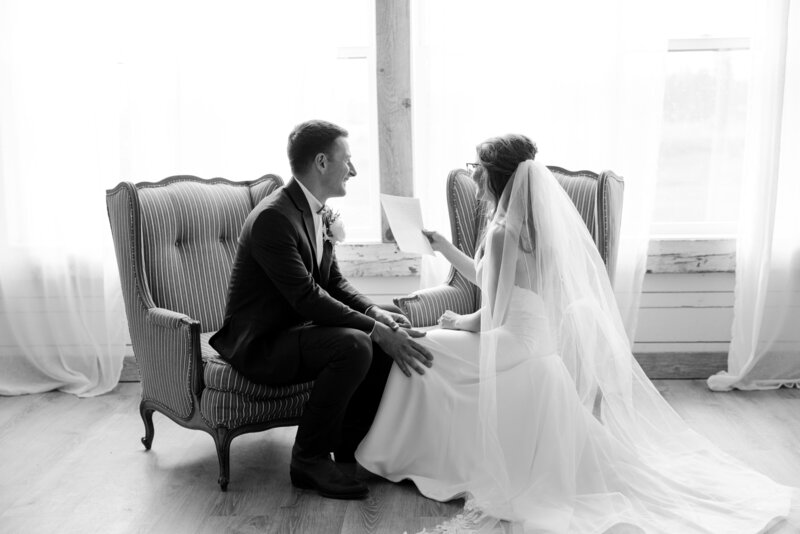 Black and white photo of bride reading vows while sitting beside her groom.