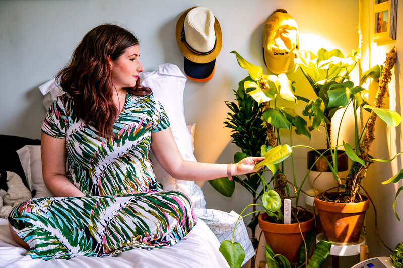 Woman sits on her bed and admires her indoor potted plants