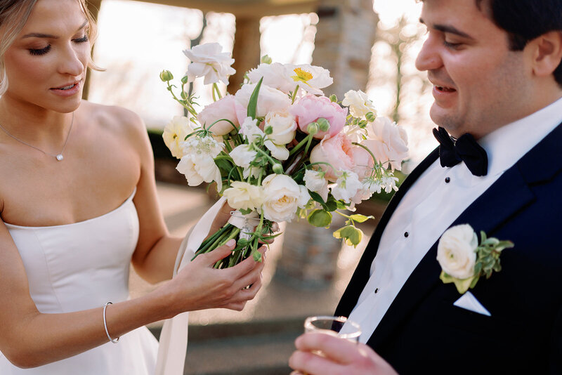 Bride showing her white and blush wedding bouquet to the groom during their ceremony at Burritt on the Mountain in Huntsville, Alabama, captured by Perry Hancock.