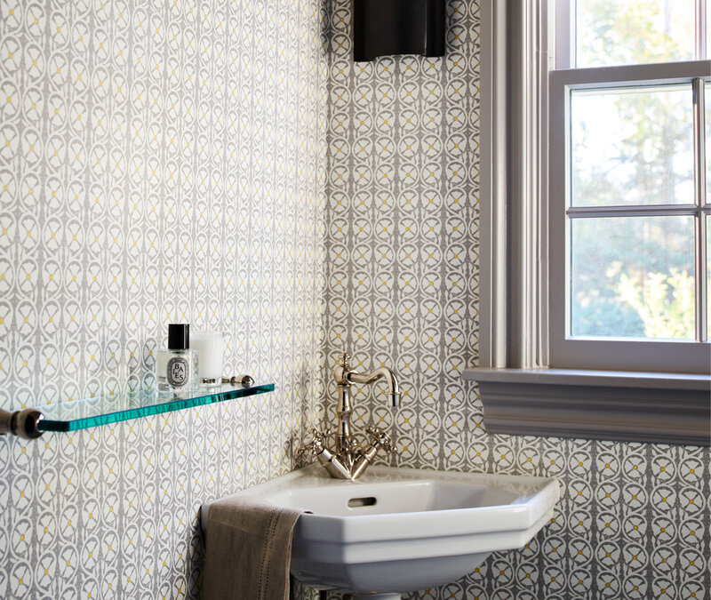 Boston interior designer creates bathroom classic home in Milton featuring a powder room with Peter Fasano wallpaper, corner sink, and glass shelf accents.