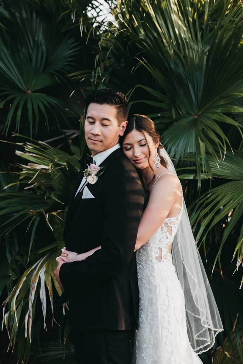 Bride hugging groom in front of green plants