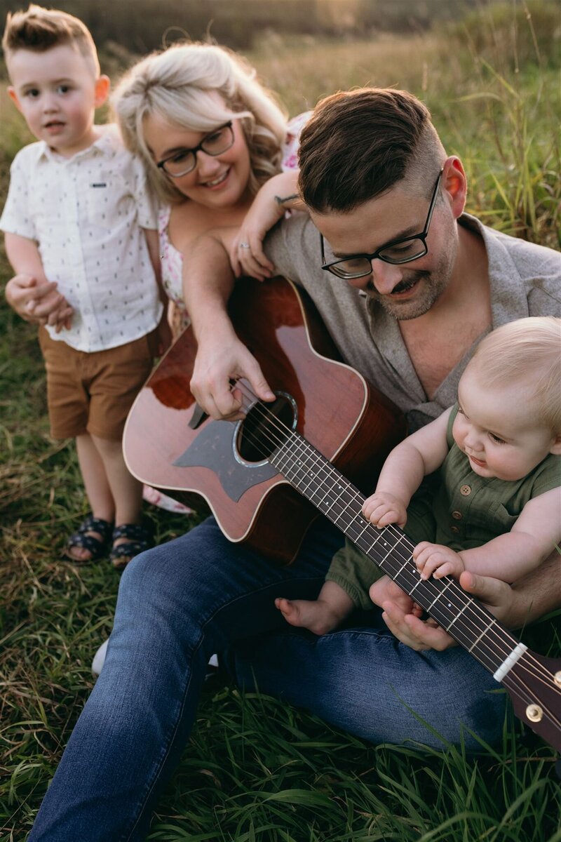 Family photo during sunset at Pinhey's Historic Point in the field with two daughters running around parents who are hugging