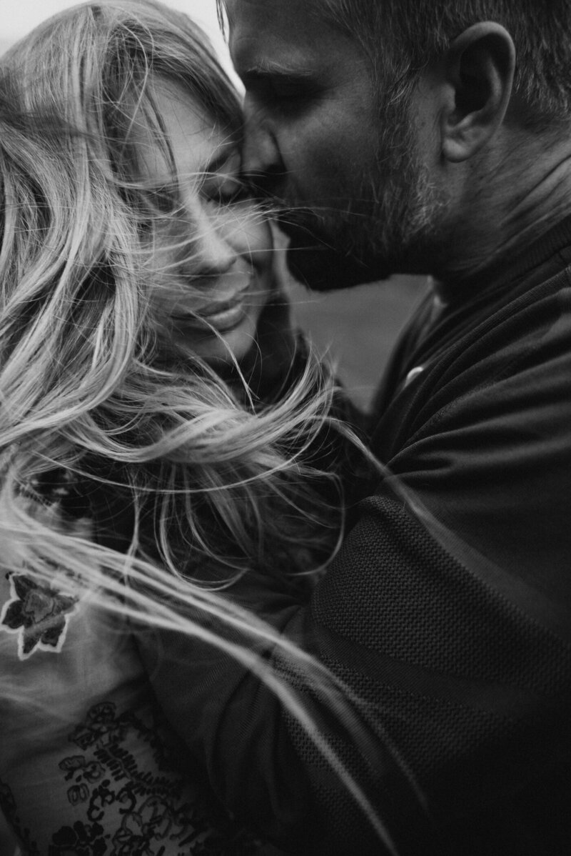 Black and white of man and woman couple kissing in the wind for engagement photos