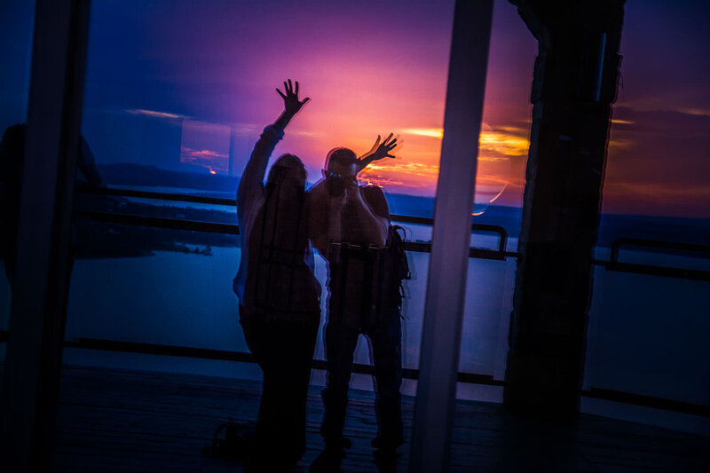 Silhouette of photographer Christopher Reynolds and wife Arleen photographing themselves at sunset, reflected in a glass window.