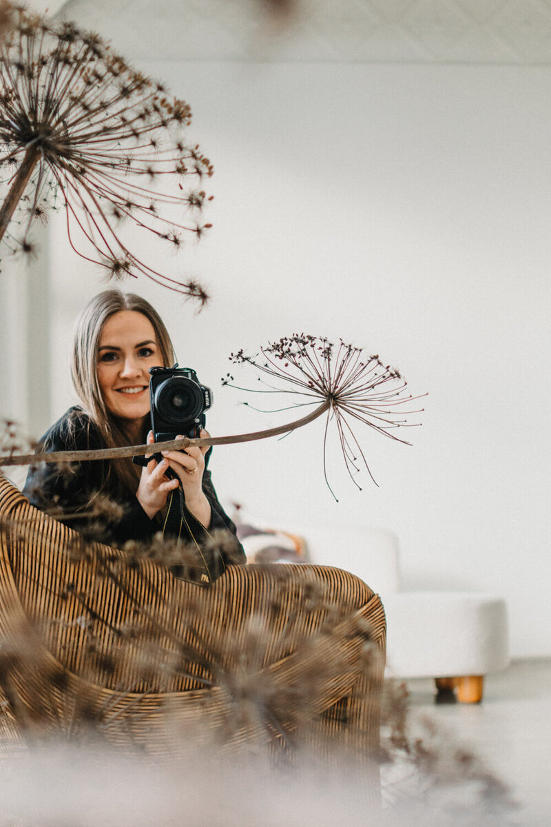 Photographer smiling while holding a camera in front of a mirror