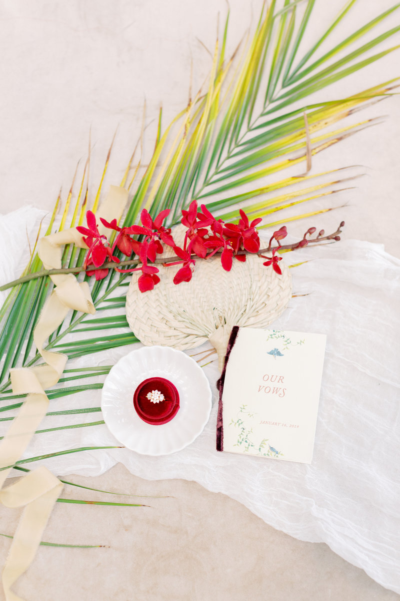 A tropical-inspired luxury wedding flat lay featuring vow books, elegant florals, and fine art details for destination brides.