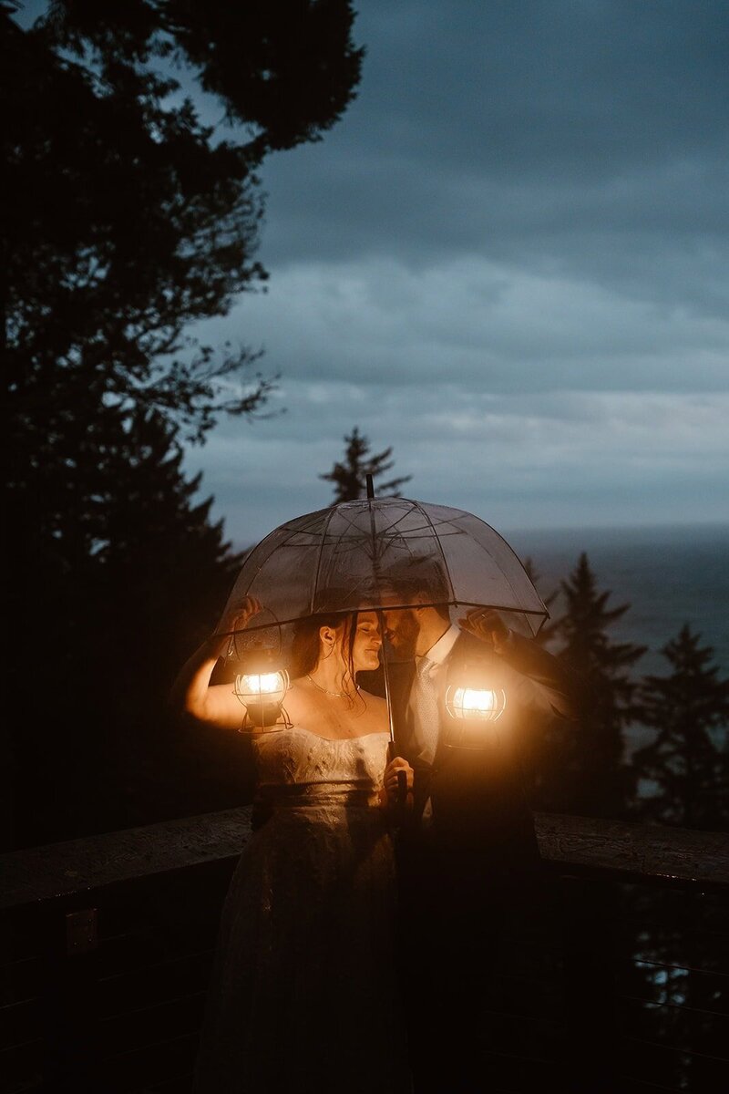 Couple holding lanterns while walking through cracked desert ground under a cloudy night sky with the moon glowing above distant mountains.